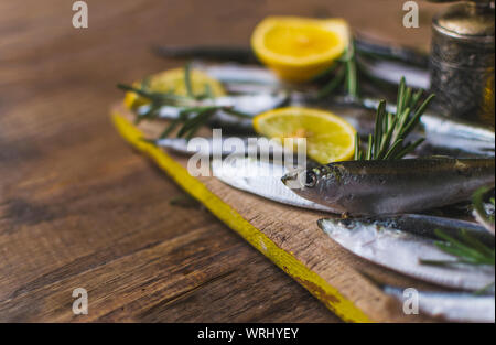 Gefrorenen Sardinen mit Zitrone und Rosmarin auf alten, dunklen, hölzernen Tisch. Stockfoto