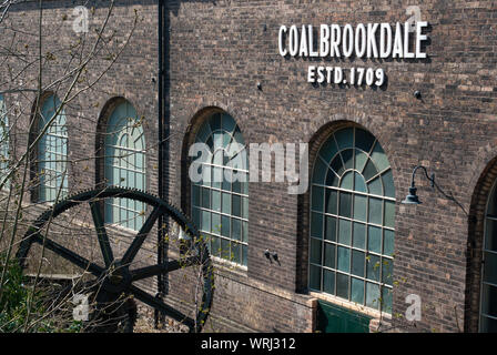 Coalbrookdale arbeitet mit einem großen gusseisernen Rad im Vordergrund und weißen Schildern auf dem Gebäude Stockfoto