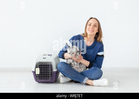 Charmante positive junge Frau hält in ihrer Hände ihre schönen grauen schottischen Katze sitzt auf dem Boden in eine neue Wohnung. Pet-Konzept. Stockfoto