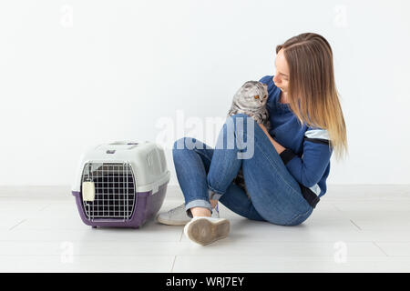 Charmante positive junge Frau hält in ihrer Hände ihre schönen grauen schottischen Katze sitzt auf dem Boden in eine neue Wohnung. Pet-Konzept. Stockfoto