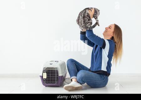 Charmante positive junge Frau hält in ihrer Hände ihre schönen grauen schottischen Katze sitzt auf dem Boden in eine neue Wohnung. Pet-Konzept. Stockfoto