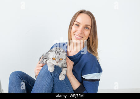 Charmante positive junge Frau hält in ihrer Hände ihre schönen grauen schottischen Katze sitzt auf dem Boden in eine neue Wohnung. Pet-Konzept. Stockfoto