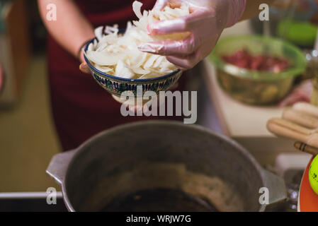 Frau setzt Zwiebeln in einer Pfanne mit Butter. Der Koch brät Zwiebeln in einer Pfanne in eine große Menge von pflanzlichem Öl Stockfoto