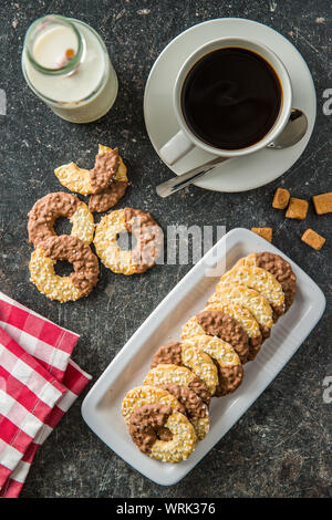 Kekse und ähnliches Kleingebäck, gesüßt Ringe. Kekse mit Schokolade und Kaffee Tasse. Ansicht von oben. Stockfoto