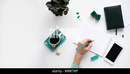 Flach, Ansicht von oben Büro Schreibtisch Schreibtisch. Arbeitsbereich mit einem weiblichen Linkshänder hand Notizen in ein Notebook, Smartphone, Schreibwaren, Bleistift, Durchfluss Stockfoto
