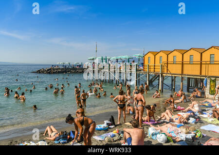 SORRENTO, ITALIEN - AUGUST 2019: Menschen auf den kleinen Strand und im Meer unterhalb der Stadt Sorrent, die an der Spitze der Klippen gelegen ist. Stockfoto