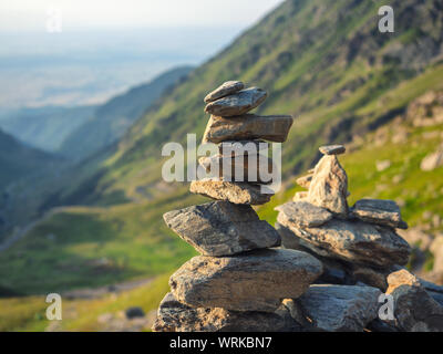 Stein mit ausgewogenen Steine auf unscharfen Hintergrund Berge im Sonnenuntergang warmes Licht Stapel Stockfoto
