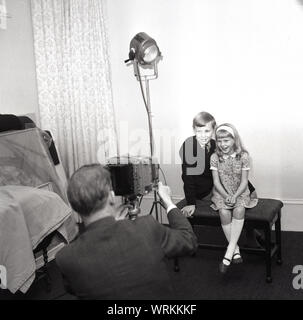 1970 s, historischen, zwei junge Kinder in einem Studio sitzen nebeneinander auf einem Hocker in Ihr Bild von einem professionellen Fotografen, England UK. Stockfoto