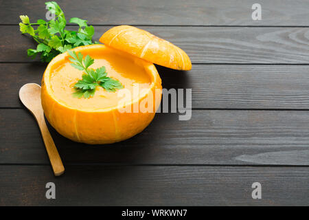 Kürbis creme Suppe in natürlichen Kürbis schälen mit Petersilie Dekoration und Löffel aus Holz Über Holz- Tabelle mit kopieren. Fallen traditionelle amerikanische Gericht Stockfoto