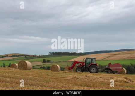 Ein Landwirt Pressen von Stroh in einem Feld in der Aberdeenshire Landschaft an einem bewölkten Nachmittag Stockfoto