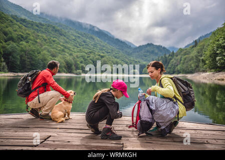 Familie mit kleinen gelben Hund ruht auf einem Pier am See und nebligen Berge Stockfoto