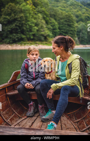 Mutter und Tochter mit einem kleinen gelben Hund sitzen in einem Boot auf dem See und im Gespräch Stockfoto