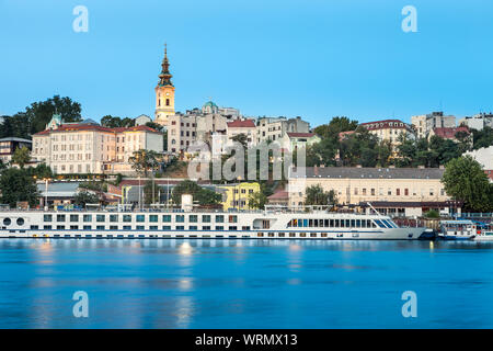 Blaue Stunde Blick auf Belgrad riverfront mit Fluss Sava im Vordergrund, heiligen Erzengel Michael Kathedrale an der Rückseite und beeindruckende Cruiser im Hafen Stockfoto