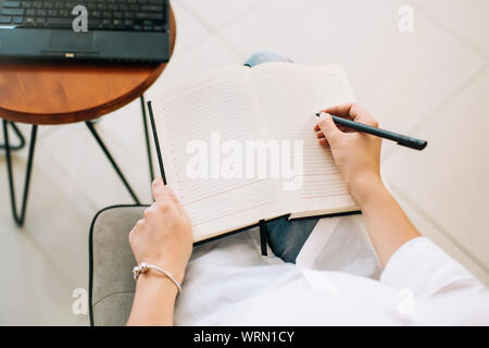 Weibliche Hände in einem Notepad schreiben, Überblick. Geschäftsfrau, die in einem gemütlichen modernen Arbeitsbereich. Stockfoto