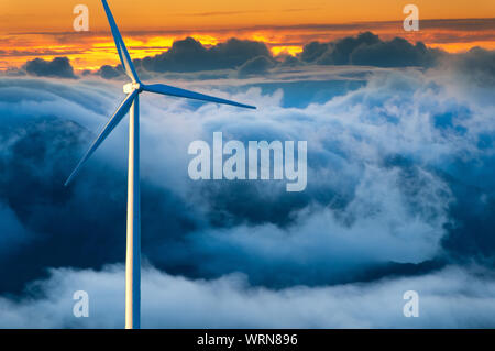Große Windenergieanlage vor einem stürmischen Wolken bei Sonnenuntergang im Hintergrund stehen. Stockfoto