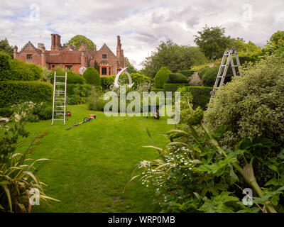 Chenies Manor formschnitt Garten mit Wartung läuft. Heckenschere, Schubkarre und Leitern sind im Einsatz auf dem Rasen. Stockfoto