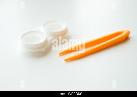 Zubehör für die richtige Verwendung von Kontaktlinsen: Gehäuse und orangefarbene Pinzette auf hellweißem Hintergrund. Sichere Sehkorrektur. Selektiver Fokus. Stockfoto