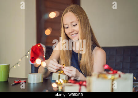 Junge Frau ist Verpackung präsentiert. Derzeitige eingewickelt in Handwerk Papier mit einer Rot und Gold Ribbon für Weihnachten oder Neujahr. Frau macht einen Adventskalender Stockfoto