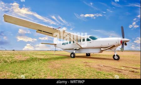 Ein weißes, single engine charter Flugzeug sitzt auf einem Gras und Schmutz Landeplatz in schöner und ruhiger Lage in Kenia Stockfoto