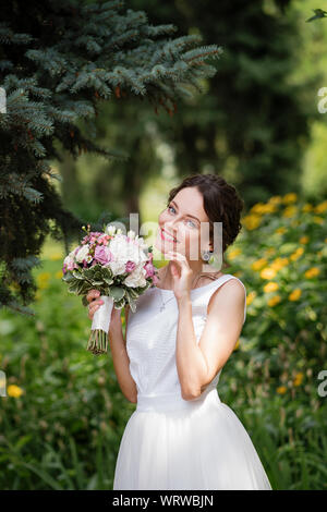 Emotionale Portrait von einer glücklichen Braut in der Mode Hochzeit Kleid auf die natürlichen Hintergrund. Frisch Verheiratete mit einem brautstrauß in der Hand lacht glücklich nach t Stockfoto