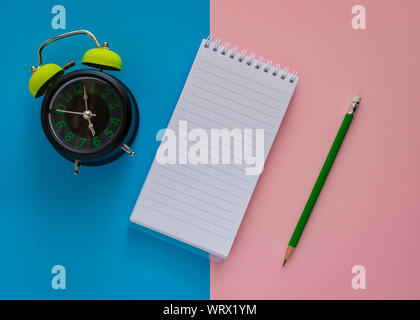 Notebook mit grünen Stift und Wecker auf Rosa und blauen Papier Hintergrund öffnen, Bildung Konzept. Stockfoto