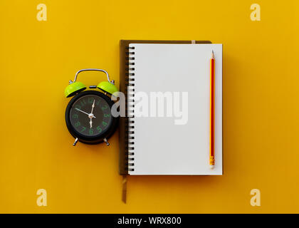 Leere weiße Notizblock mit Stift und Wecker auf gelbem Hintergrund, Bildung inspiration Konzept. Stockfoto