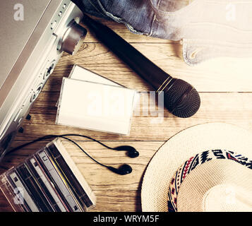 Satz von Audio Device, Mikrofon, Kopfhörer, Kassette, denim Tasche und Hut auf Holz- vintage Hintergrund Stockfoto