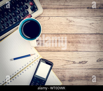 Büro Schreibtisch Hintergrund. Kaffee, Notizblock, Bleistift, Mobiltelefon und Schreibmaschine auf vintage Schreibtisch aus Holz Stockfoto