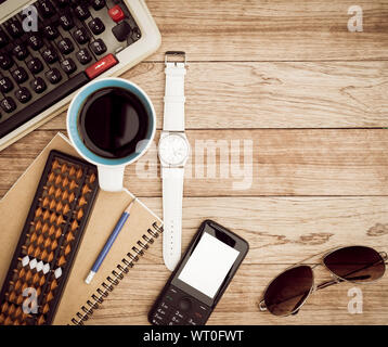 Büro Schreibtisch Hintergrund. Kaffee, Notizblock, Bleistift, Armbanduhr, Handy, Sonnenbrille, Abacus und Schreibmaschine auf vintage Schreibtisch aus Holz Stockfoto