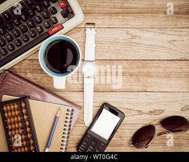 Büro Schreibtisch Hintergrund. Kaffee, Notizblock, Bleistift, Armbanduhr, Buch, Handy, Sonnenbrille, Abacus und Schreibmaschine auf vintage Schreibtisch aus Holz Stockfoto