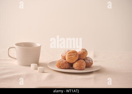 Donuts mit Zucker auf dem Teller und Tasse Kaffee auf weißem Hintergrund Stockfoto