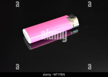Ein rosafarbenes Kunststofffeuerzeug liegt auf einer glänzend schwarzen Oberfläche. Stockfoto