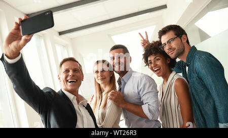 Glückliche Momente. Gruppe von Kolleginnen und Kollegen unter selfie lächelnd und deutete, während im modernen Büro. Fotografie Konzept. Büroalltag. Stockfoto