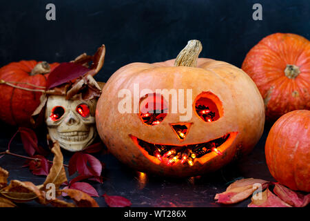 Halloween kreative Komposition mit einem Schädel und ein Scary Pumpkin auf dunklem Hintergrund, Nahaufnahme, horizontale Ausrichtung Stockfoto