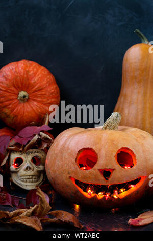 Halloween kreative Komposition mit einem Schädel und ein Scary Pumpkin auf dunklem Hintergrund, Nahaufnahme, vertikale Ausrichtung Stockfoto