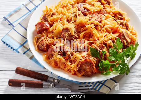 In der Nähe von Kohl Eintopf mit in Scheiben geschnittenen gegrillte Würstchen auf einem weißen Teller auf einen hölzernen Tisch serviert, horizontale Ansicht von oben Stockfoto
