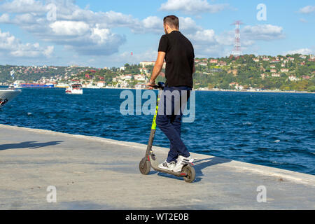 Junger Mann, Marti Tech, Motorrollerverleih, vermietet Elektroroller am Meer. Blick auf den Bosporus mit Wolken im Hintergrund. Stockfoto