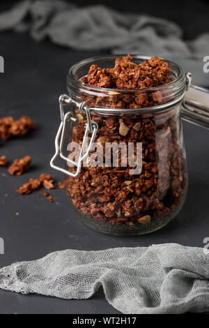 Müsli knuspriges Müsli mit natürlichem Honig, Schokolade und Nüsse in einem Glas vor einem dunklen Hintergrund, gesundes Essen, vertikale Ausrichtung Stockfoto