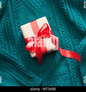 Geschenkbox in Handwerk Papier mit rotem Band auf gestrickte Oberfläche verpackt. Ansicht von oben. Quadratisches Bild. Stockfoto