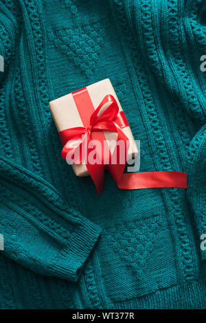 Geschenkbox in Handwerk Papier mit rotem Band auf gestrickte Oberfläche verpackt. Ansicht von oben. Ansicht von oben. Stockfoto