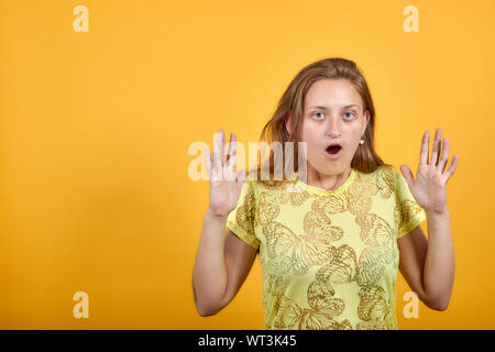 Brunette Mädchen in gelben T-Shirt über isolierte orange Hintergrund zeigt Emotionen Stockfoto