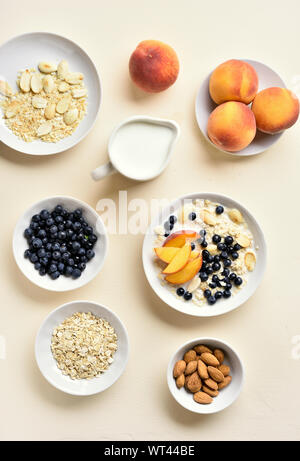 Haferflocken Porridge mit Pfirsich Scheiben-, Mandel- und wilden Blaubeeren über Licht Stein Hintergrund. Gesunde Ernährung frühstück Konzept. Ansicht von oben, flach Stockfoto