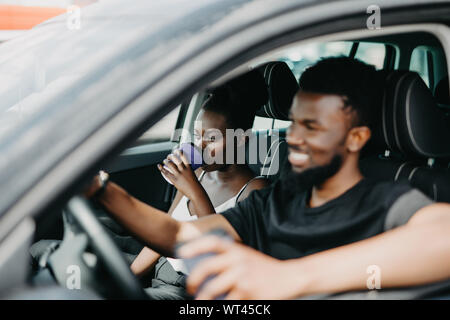 Junge afrikanische Ehepaar im Auto sitzen. Afrikanische Frau trinkt Kaffee am Morgen, während man das Auto zu arbeiten Stockfoto