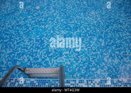 Nahaufnahme von einem blauen Pool mit blauen Mosaikfliesen auf den Pool und die Leiter hinunter zum Wasser. Stockfoto