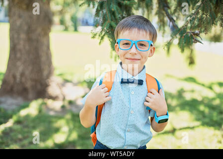 Portrait von Clever Happy Boy in Gläsern im Hemd, Schmetterling und Rucksack. Zum ersten Mal in die Schule. Zurück zu Schule. Smart wenig Schüler. Konzept von Lea Stockfoto