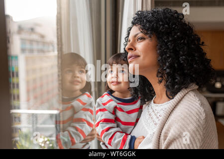 Mutter und niedlichen Tochter durch ein Fenster zu hause suchen Stockfoto