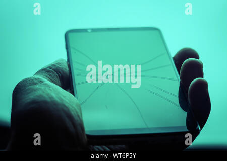 Nahaufnahme einer Hand, die ein smart phone mit Rissen auf Glas Stockfoto