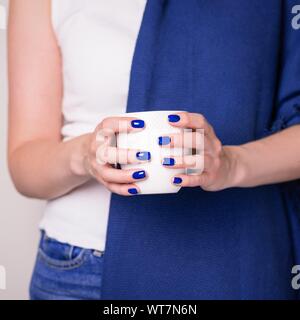 Schöne weibliche Hände halten weiße Tasse. Maniküre mit Deep Blue Nagellack. Saison ändern Konzept Stockfoto