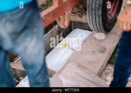 Pallbearers sorgfältig den Prozess der Senkung der Schatulle auf den Boden für die Verstorbenen an seinen endgültigen Ort der Ruhe beaufsichtigen, während der Beerdigung Stockfoto