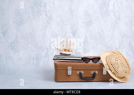 Altmodische leder Reisetasche mit Sommer marine Zubehör: Gläser, Stroh Beach Hut, Spielzeug Segelboot auf grauem Hintergrund. Banner mockup mit Kopie sp Stockfoto